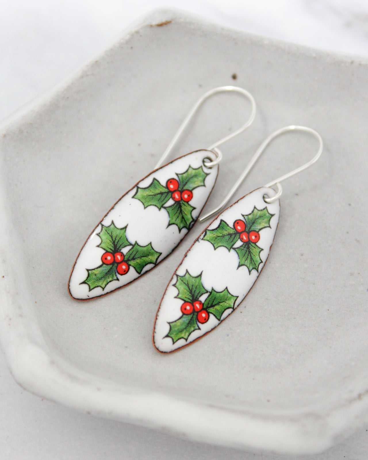 A pair of white earrings with red berries and holly leaves on a white plate.