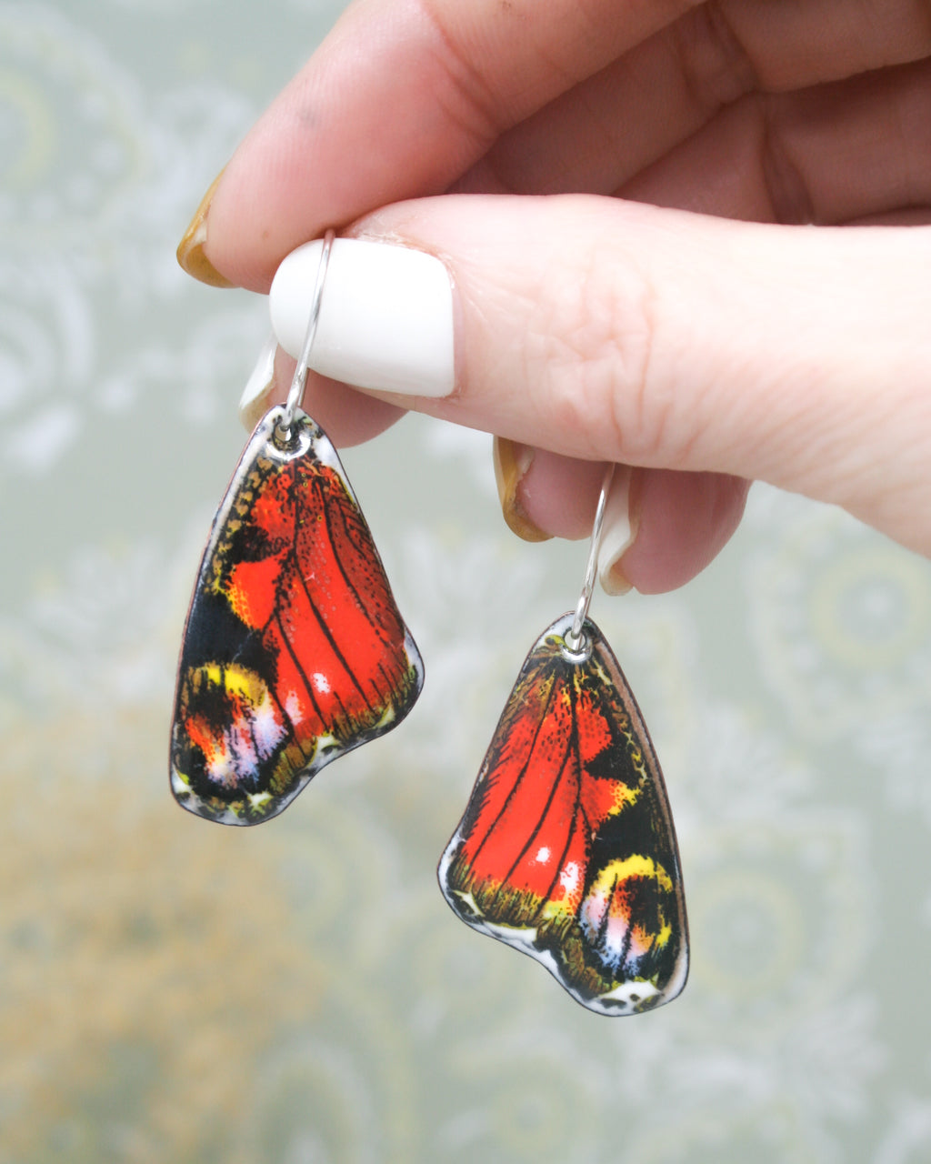 a hand holding a pair of earrings with a butterfly on it