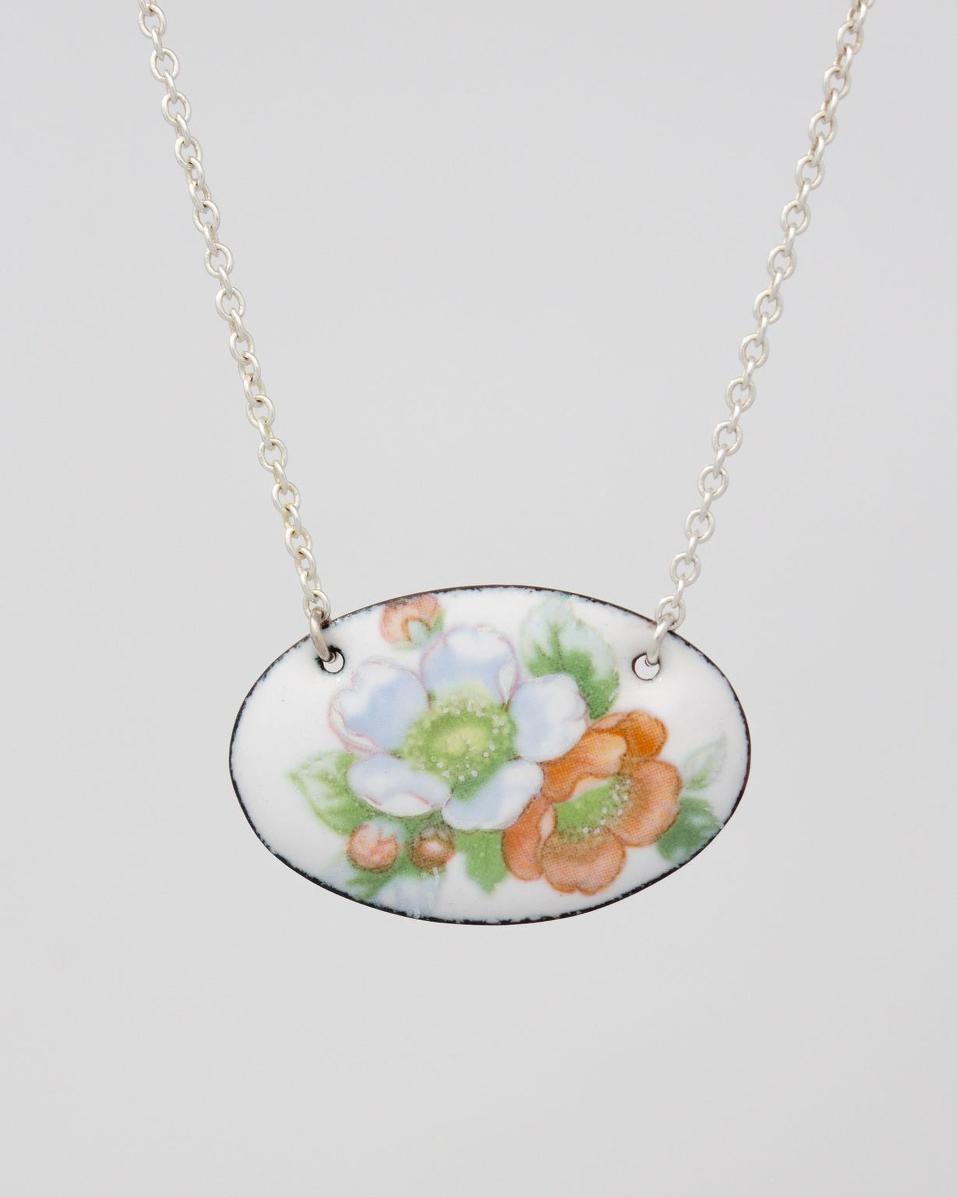 A necklace with a pendant featuring a floral design in white, orange, and green colors.