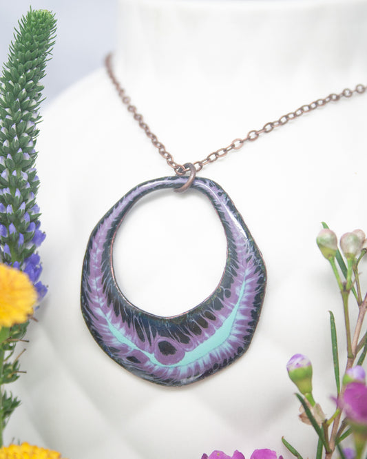 A necklace with a large, circular pendant featuring a purple and black design hangs around a person's neck.