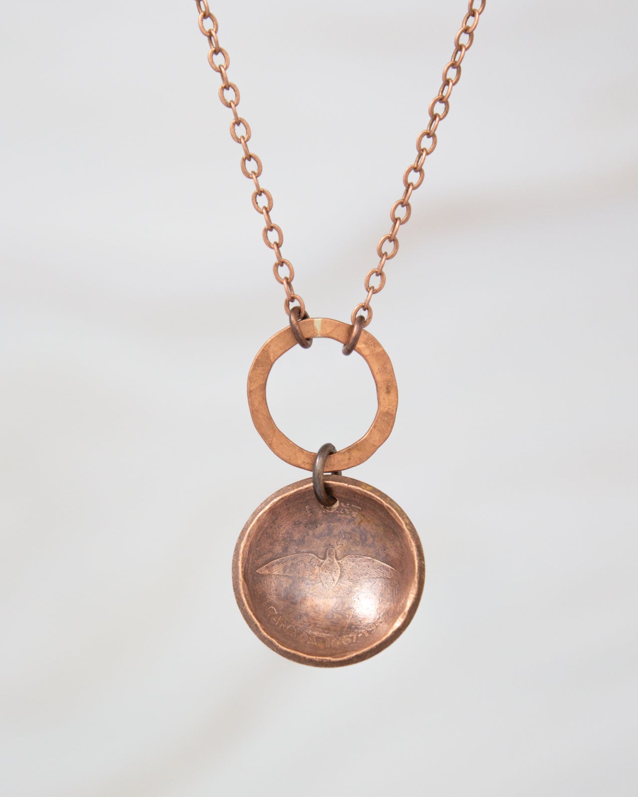 A copper-colored necklace with a circular pendant featuring a bird design.