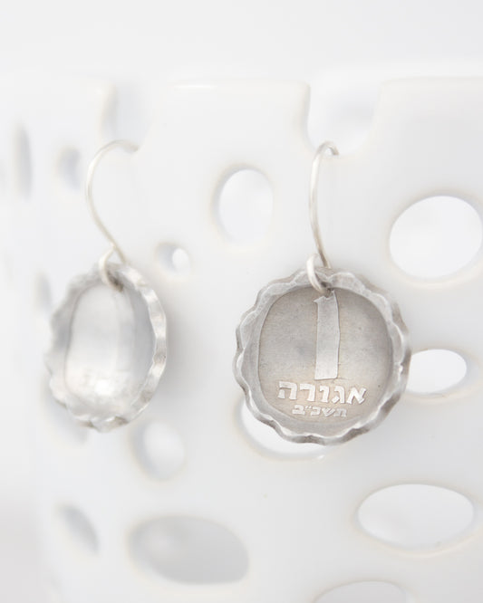 a pair of silver earrings hanging on a white surface.
