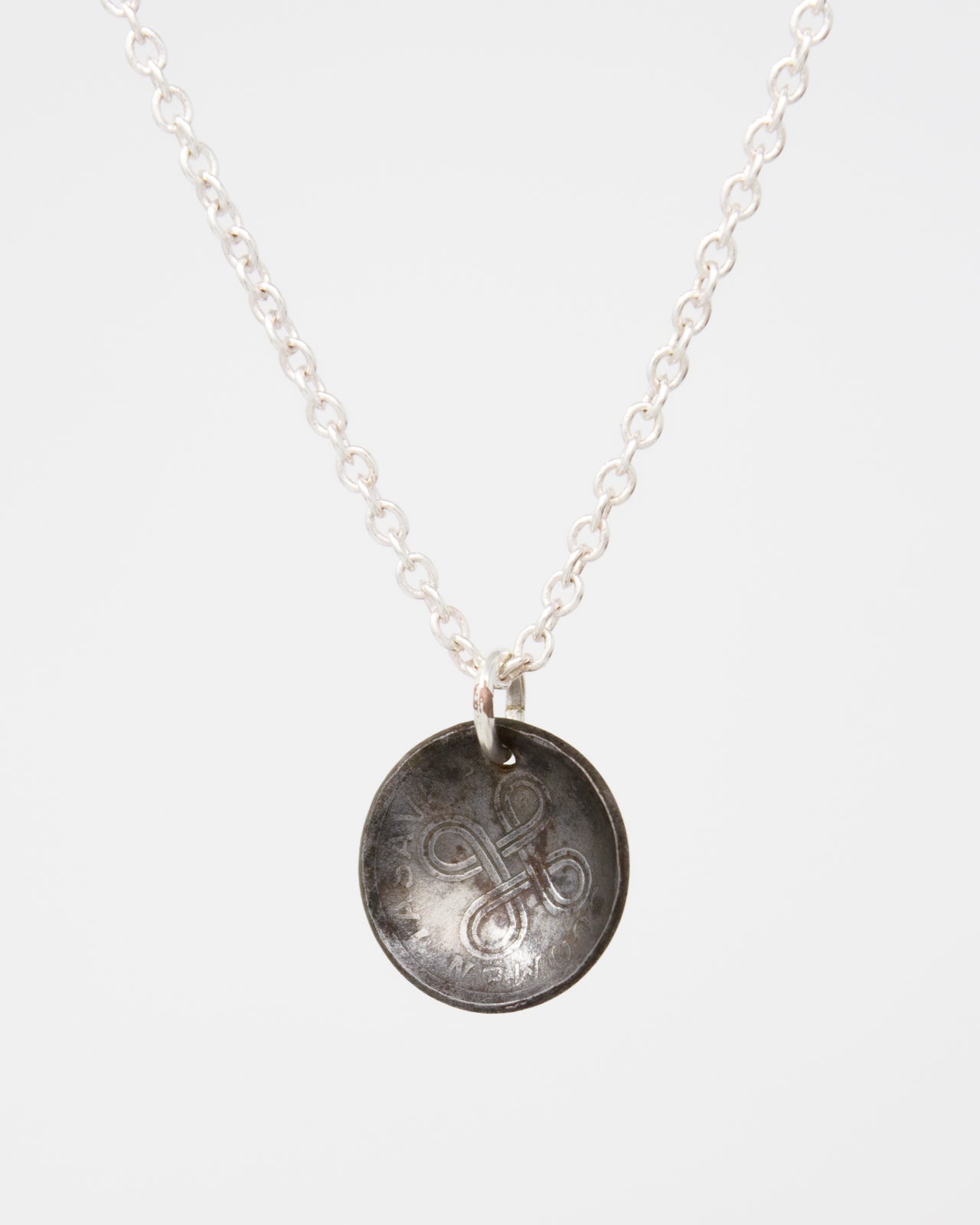 A silver necklace with a circular pendant featuring an engraved design.