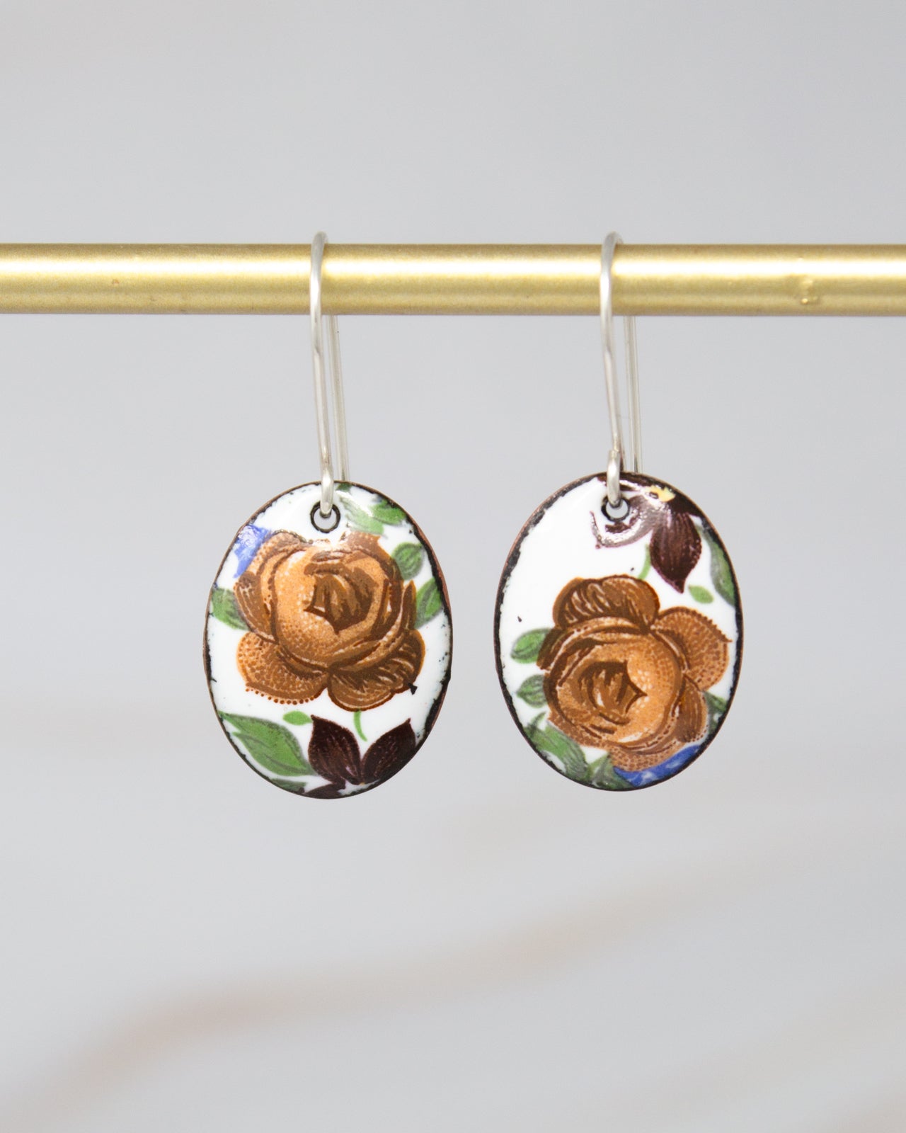 A pair of oval-shaped earrings with a floral design, hanging from a gold-colored metal hook.