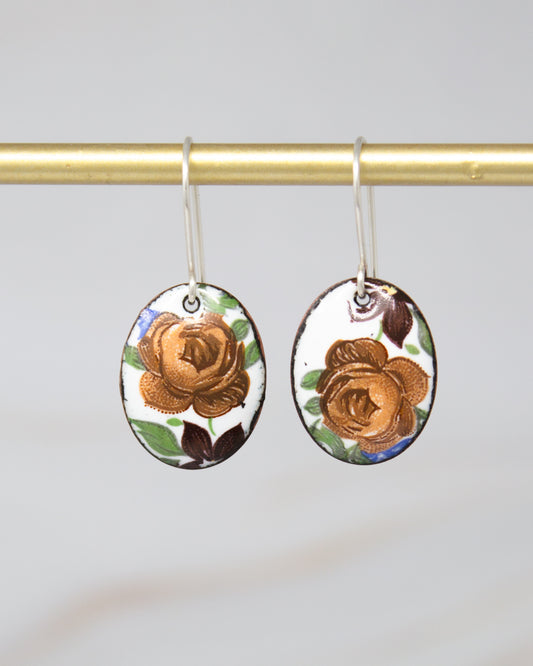 A pair of oval-shaped earrings with a floral design, hanging from a gold-colored metal hook.