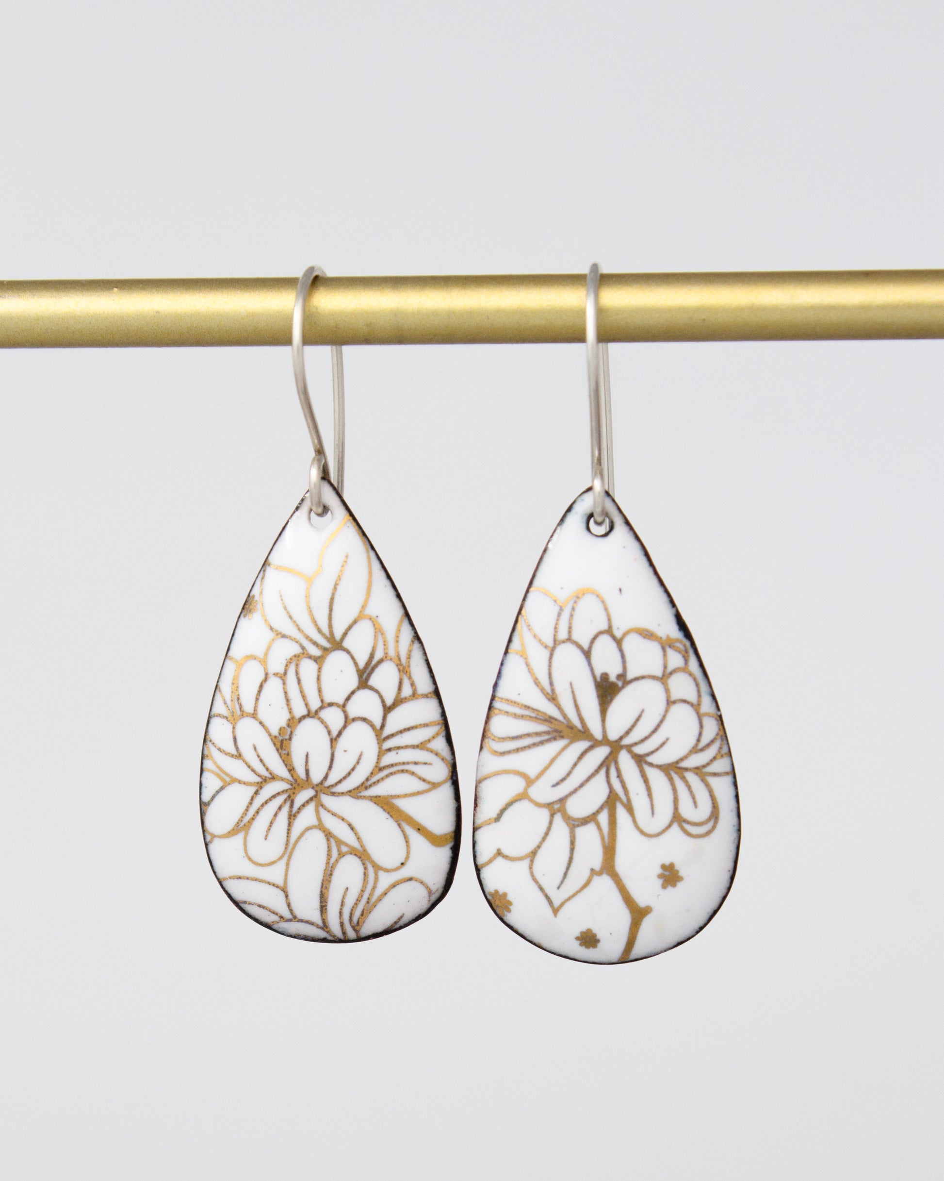 A pair of white earrings with gold floral designs hanging from a gold bar.