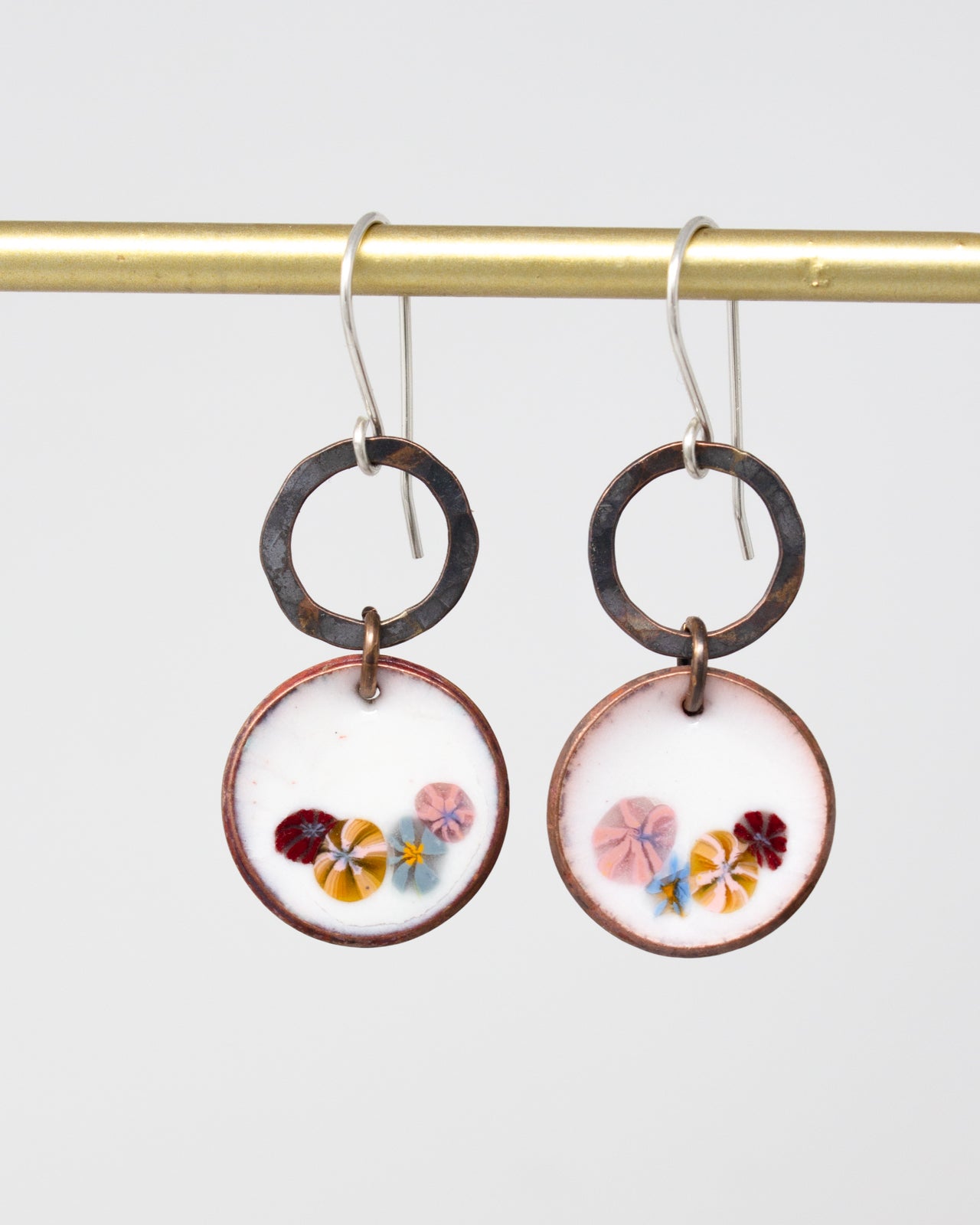 A pair of earrings with a floral design on the center, featuring a combination of pink, blue, and yellow flowers.