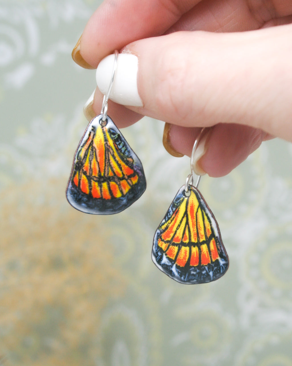 a hand holding a pair of earrings with a butterfly on it