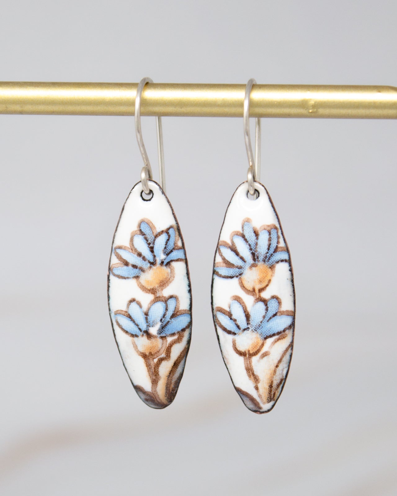 A pair of earrings with blue and brown floral designs hanging from a gold-colored metal hook.