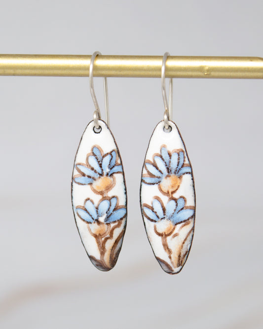 A pair of earrings with blue and brown floral designs hanging from a gold-colored metal hook.