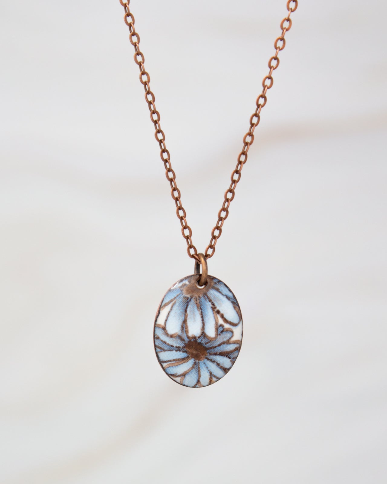 A delicate necklace with a pendant featuring a blue and white floral design.