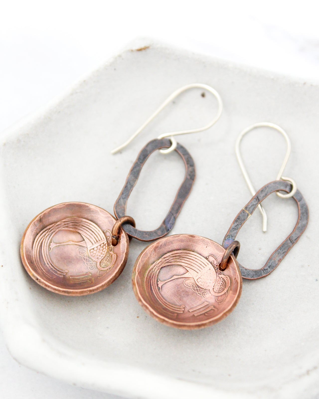 A pair of copper-colored earrings with intricate designs, resting on a white surface.