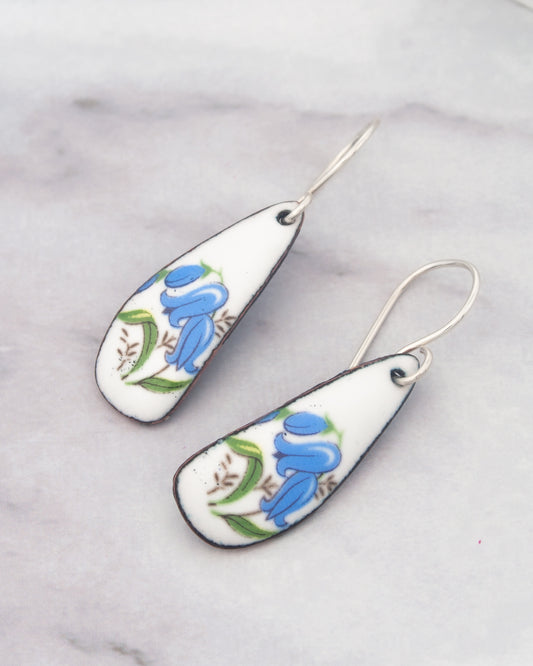 A pair of white earrings with blue floral designs on them.