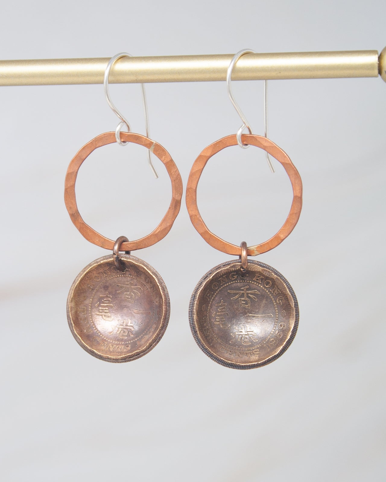 A pair of earrings with a circular design and a metal-like appearance, hanging from a hook.
