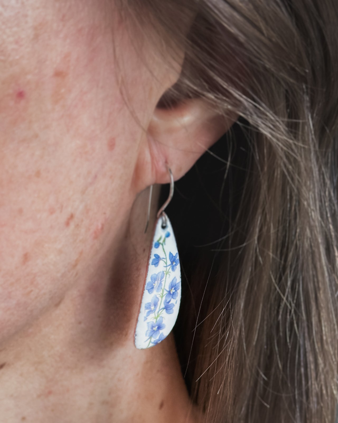 A close-up view of a person's ear with a floral earring hanging from the earlobe.