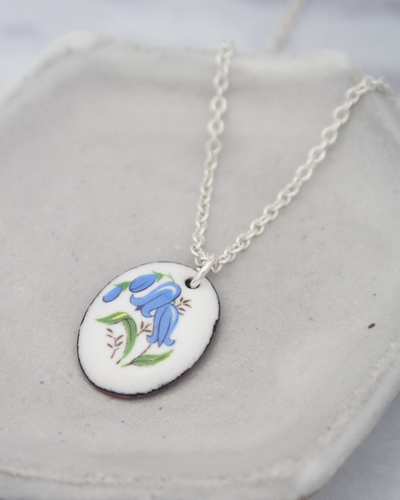 A silver necklace with a pendant featuring a blue flower design.