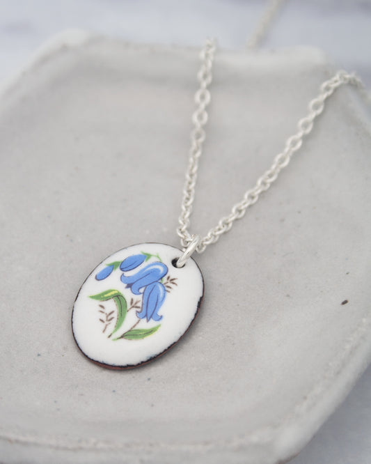 A silver necklace with a pendant featuring a blue flower design.
