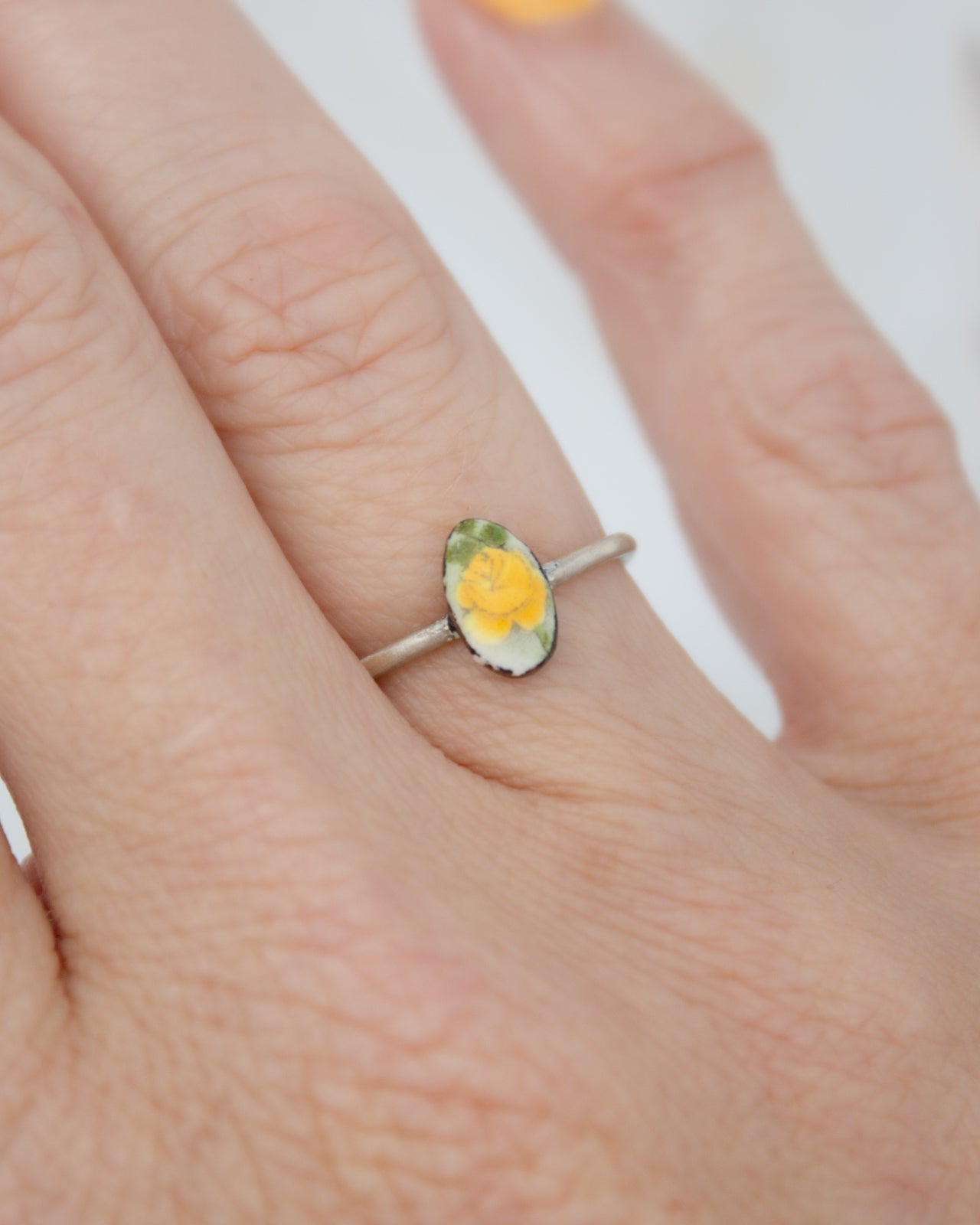 A close-up of a person's hand wearing a ring with a yellow flower on it.