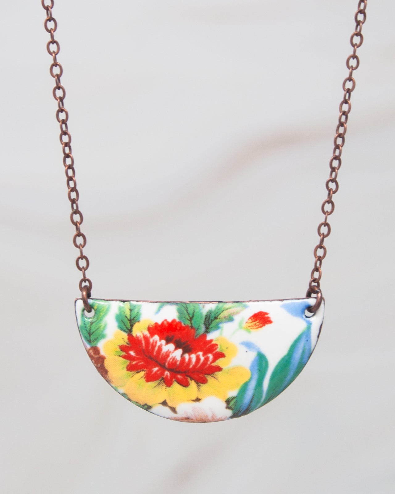 A colorful pendant necklace with a floral design on a chain.