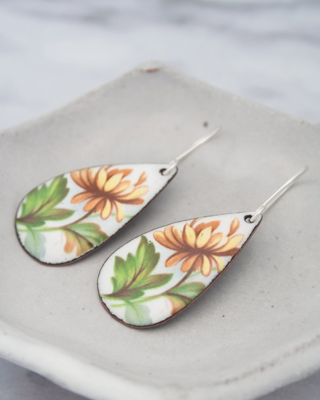A pair of earrings with a floral design, featuring yellow and orange flowers on a white background.