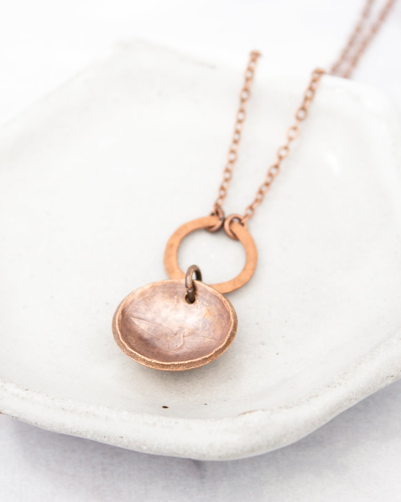 A copper-colored necklace with a round pendant is displayed on a white surface.