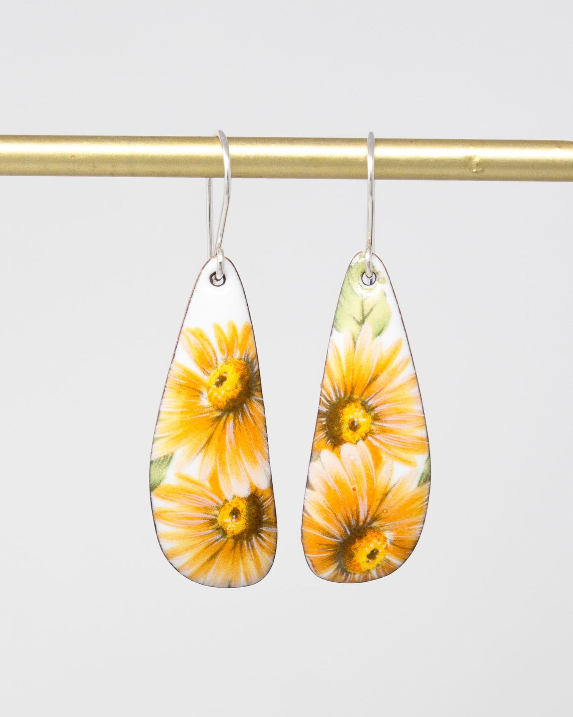 A pair of earrings with yellow sunflower designs hanging from a gold-colored metal bar.