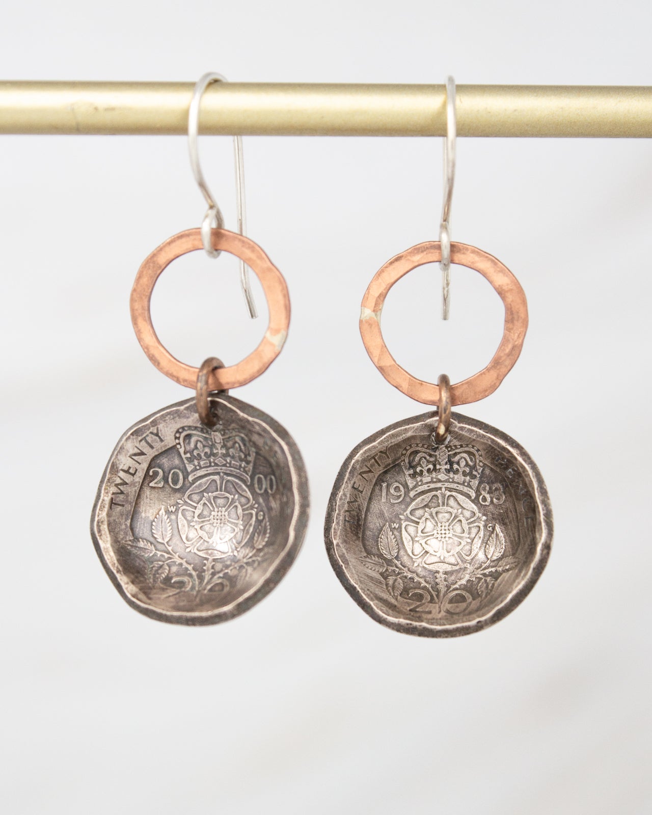 A pair of earrings made from a silver-colored metal, featuring a circular design with a copper-colored ring around it. The earrings appear to be made from a coin or similar small, metallic object.