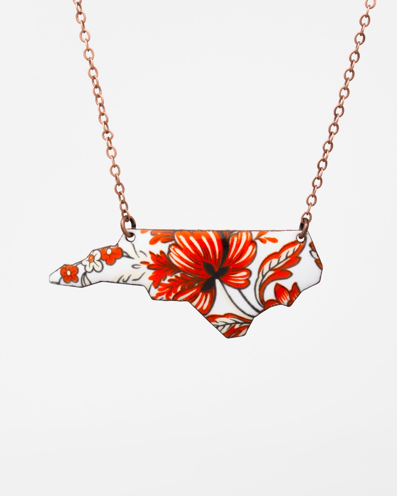 A necklace with a pendant in the shape of the state of North Carolina, featuring a floral design in red and white colors.