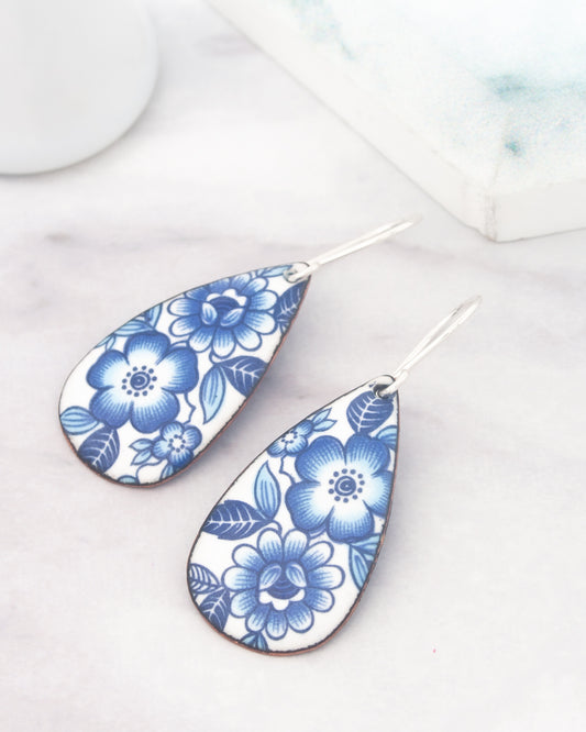 a pair of earrings with a blue floral design on a white background.