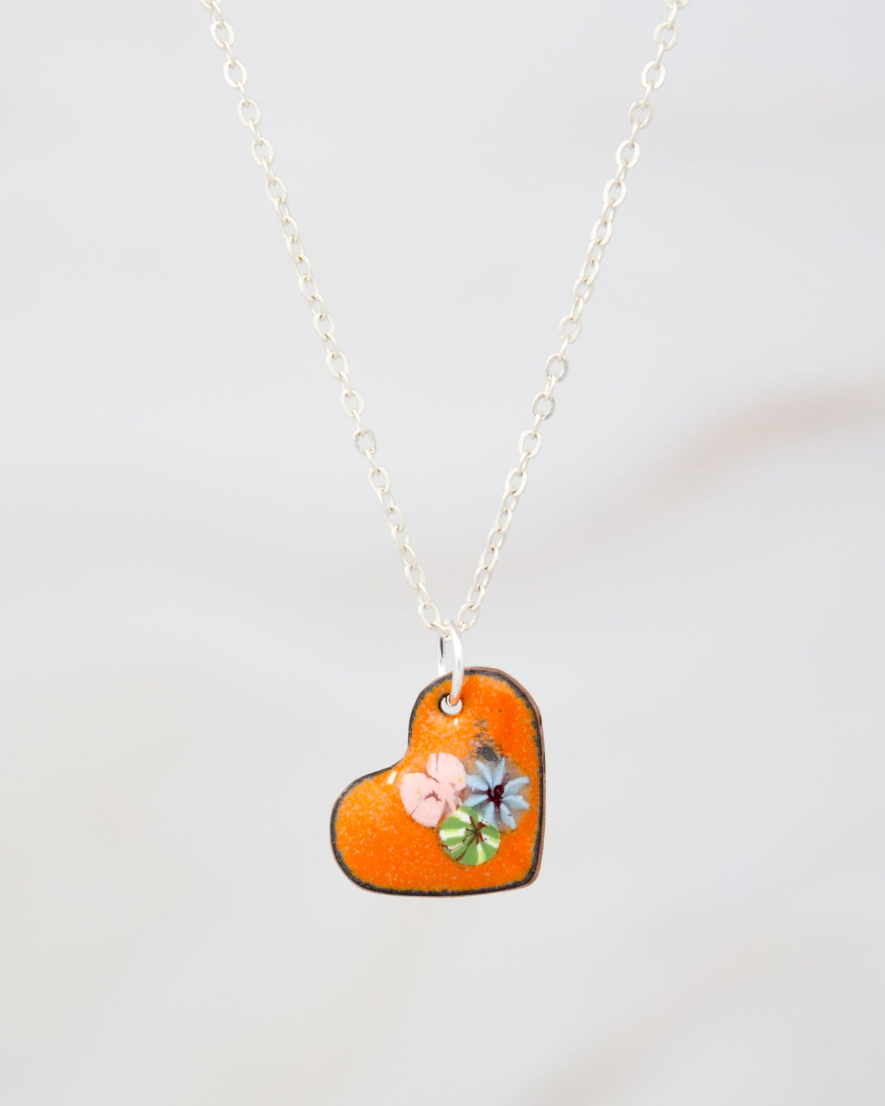 A heart-shaped pendant necklace with a small orange heart and colorful flowers attached to it.