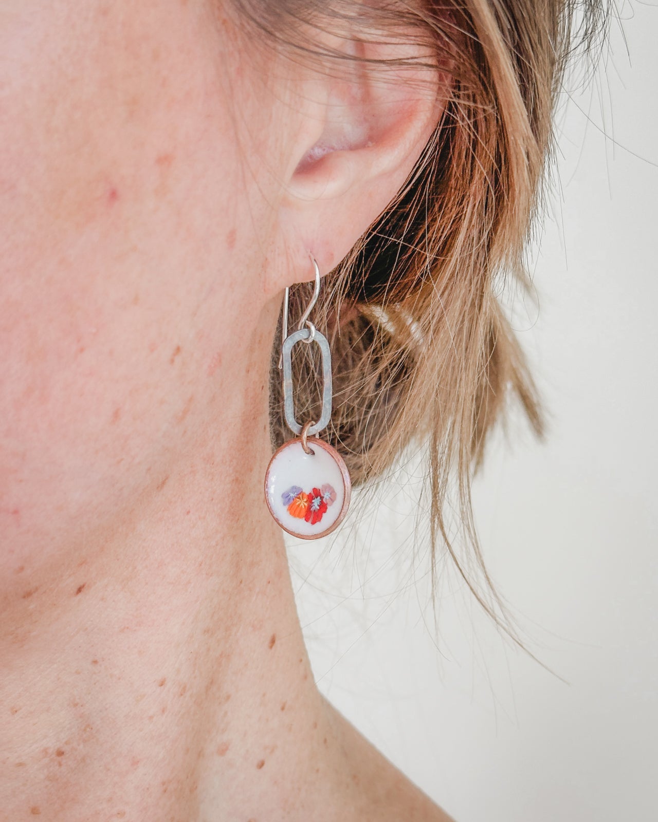 A close-up view of a person's ear wearing a pair of silver earrings with a small flower-like charm hanging from the earring hook.