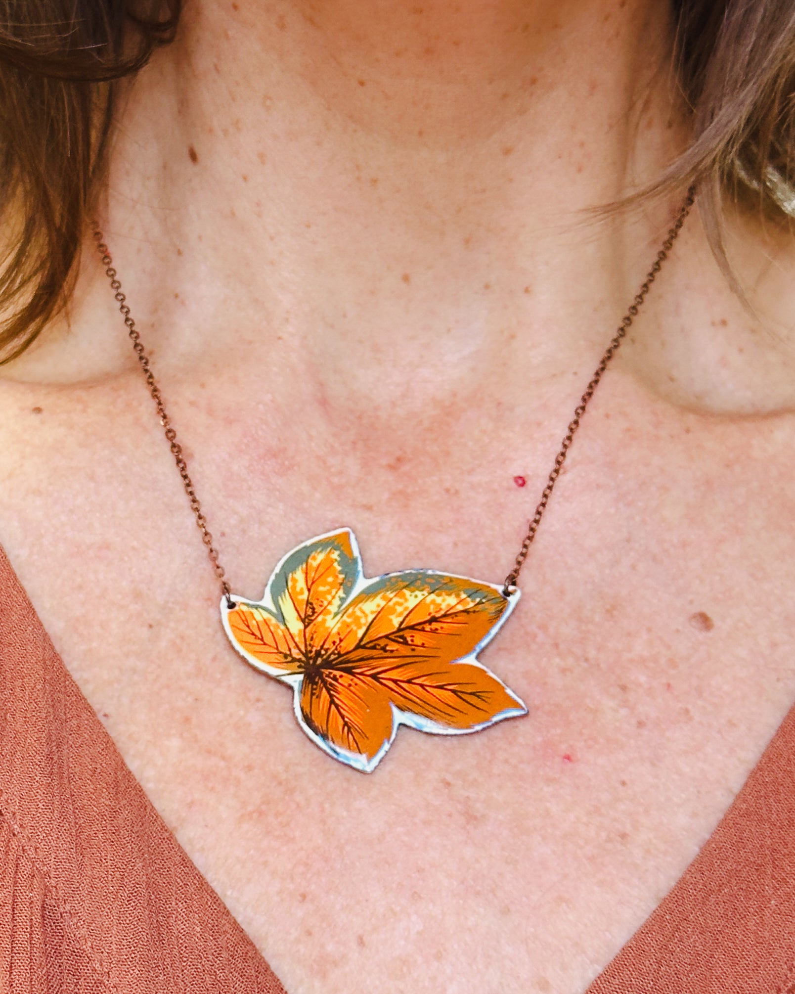 a woman wearing a necklace with an orange leaf on it