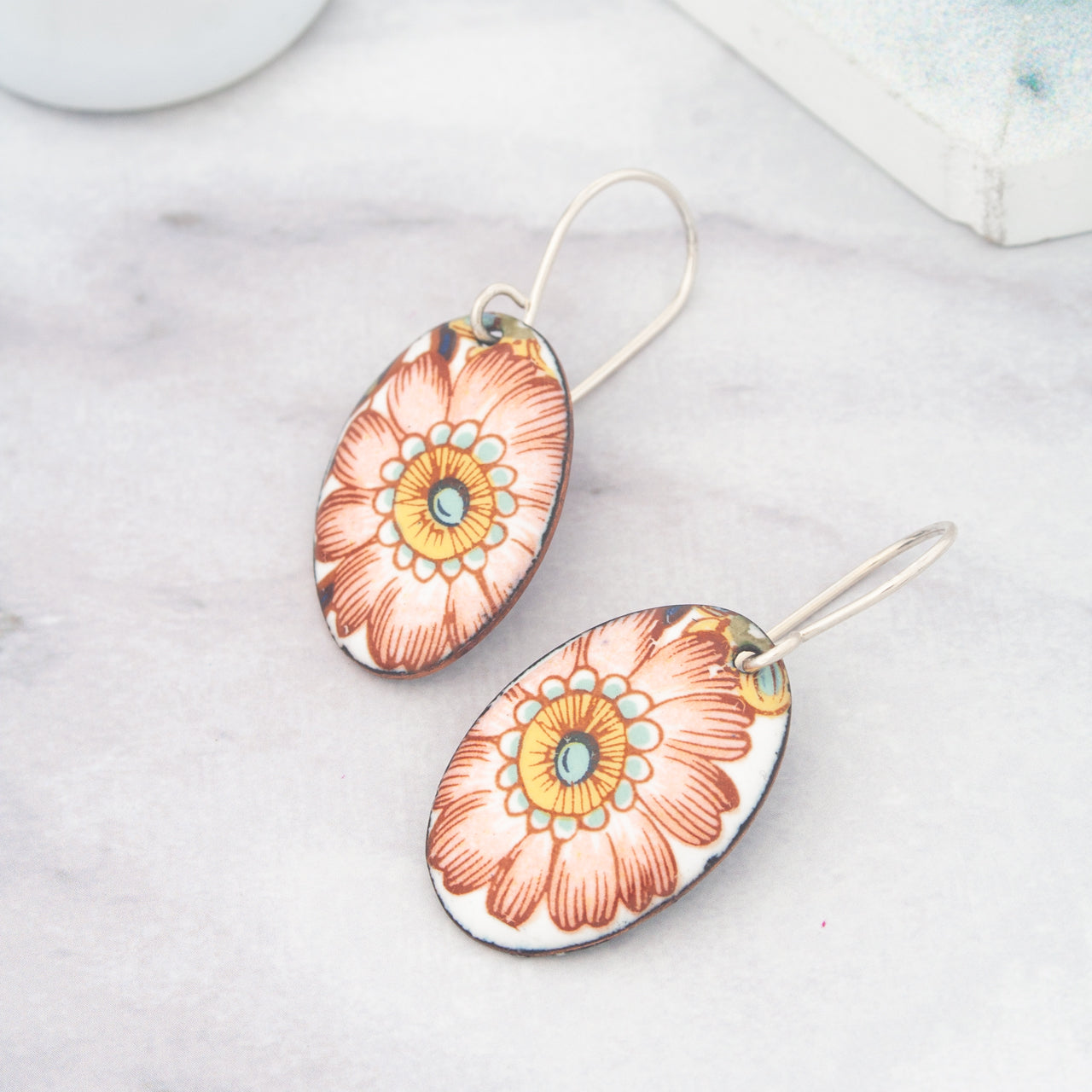 A pair of earrings with a floral design, featuring a large orange flower with a yellow center and red petals.