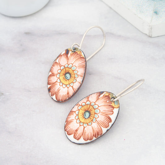 A pair of earrings with a floral design, featuring a large orange flower with a yellow center and red petals.