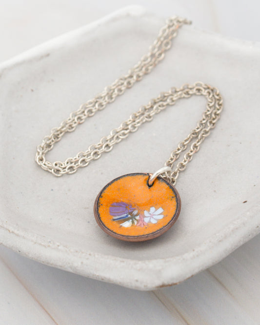 A necklace with an orange pendant featuring a floral design rests on a white surface.