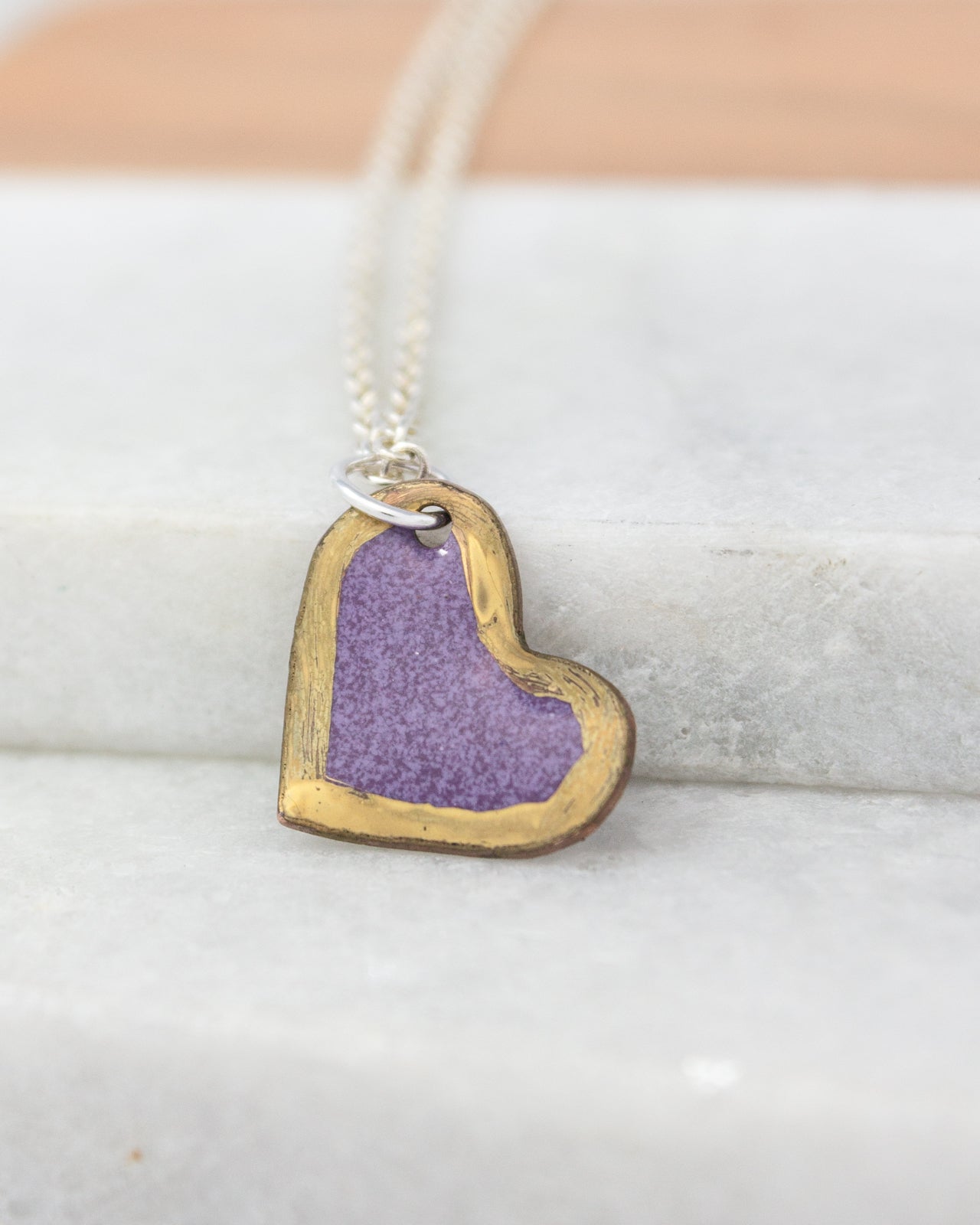 A heart-shaped pendant with a purple background and a gold border is hanging from a silver chain.
