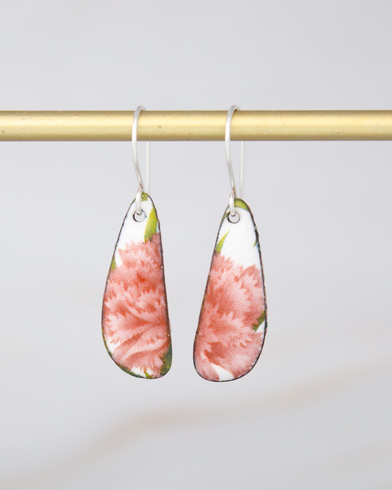 A pair of earrings with a floral design, hanging from a gold-colored metal bar.