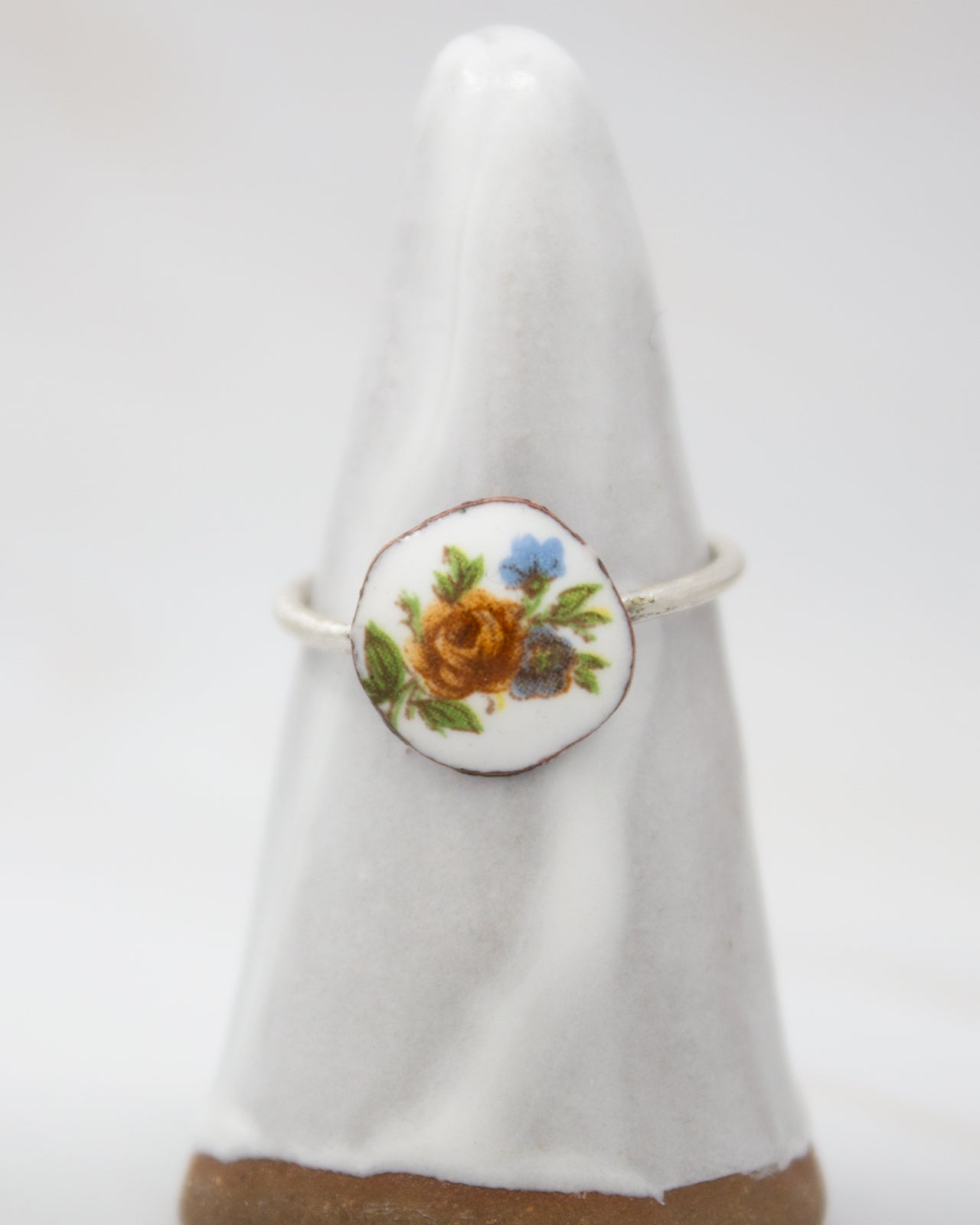 A white ceramic ring with a floral design on it, placed on a white pedestal.