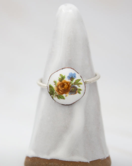 A white ceramic ring with a floral design on it, placed on a white pedestal.