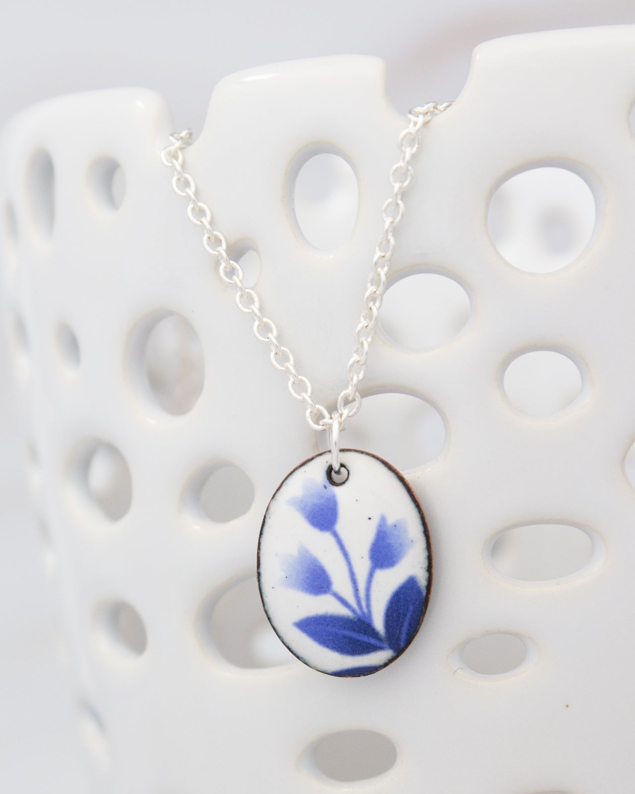 A white ceramic container with a silver chain necklace featuring a blue floral pendant.