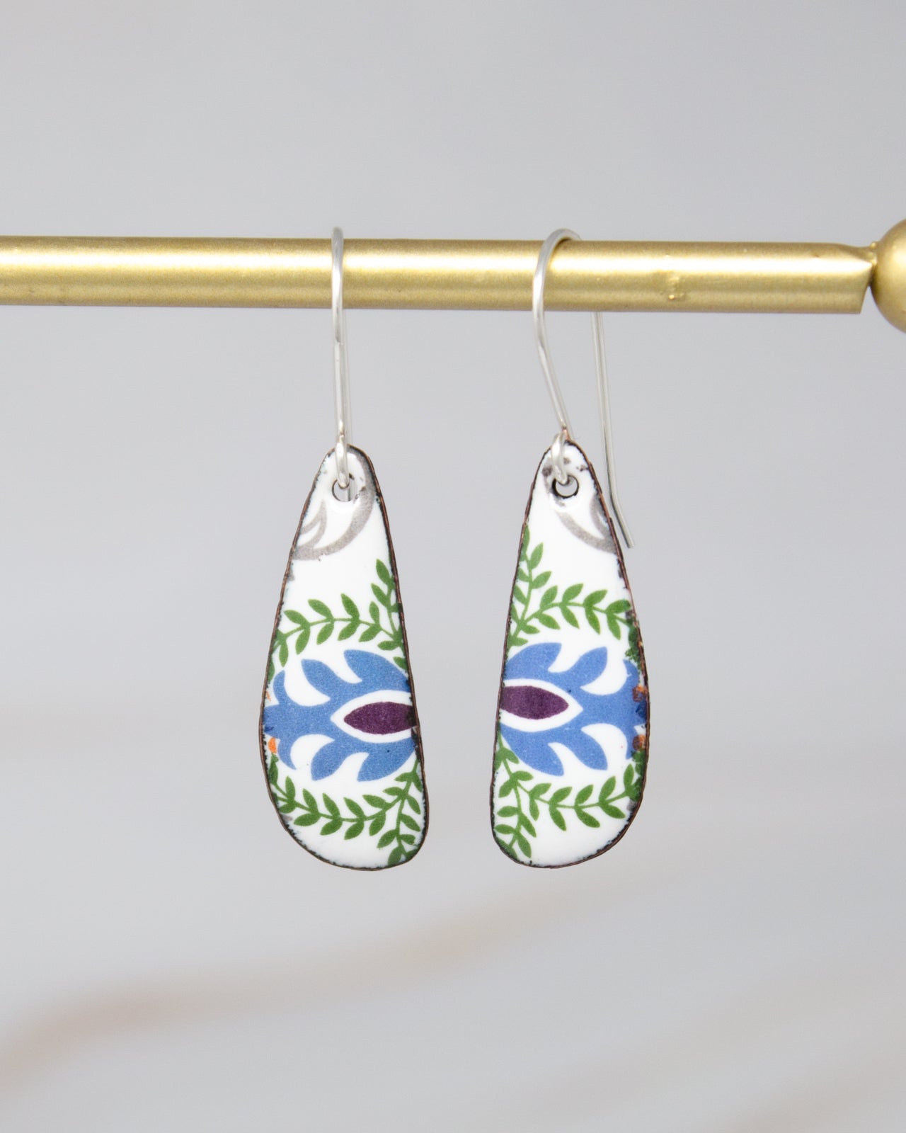 A pair of earrings with a floral design hanging from a gold-colored metal hook.
