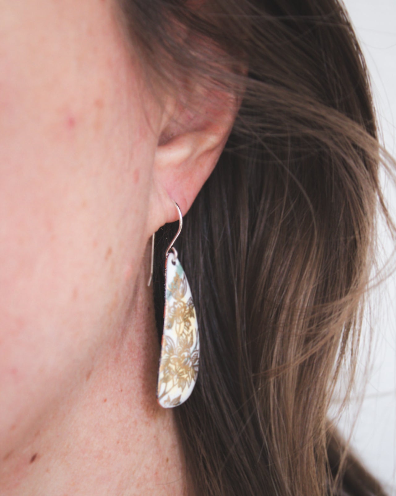 A close-up view of a person's ear wearing a pair of earrings with a floral pattern.