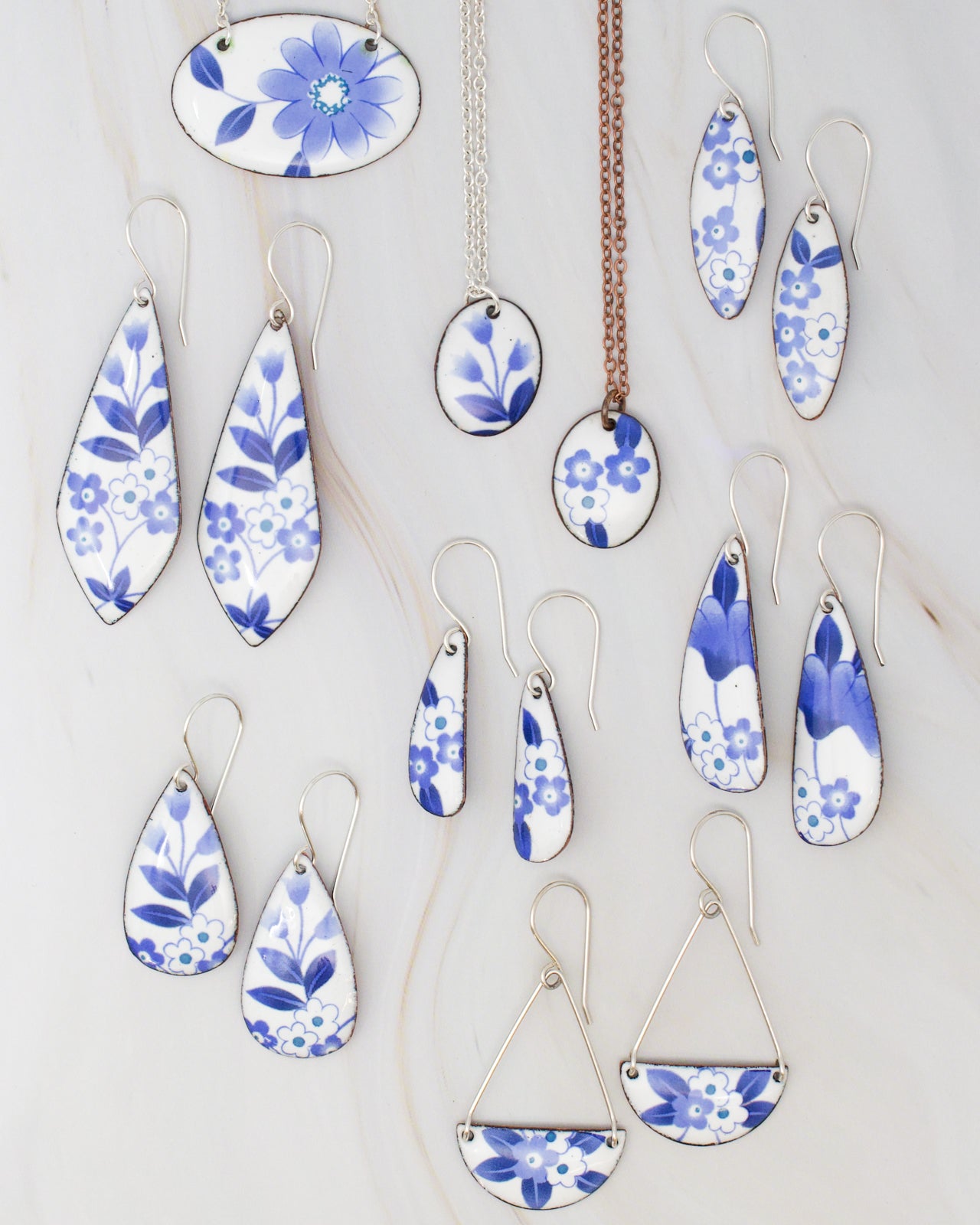 a collection of blue and white floral-patterned earrings and pendants, arranged on a marble surface.