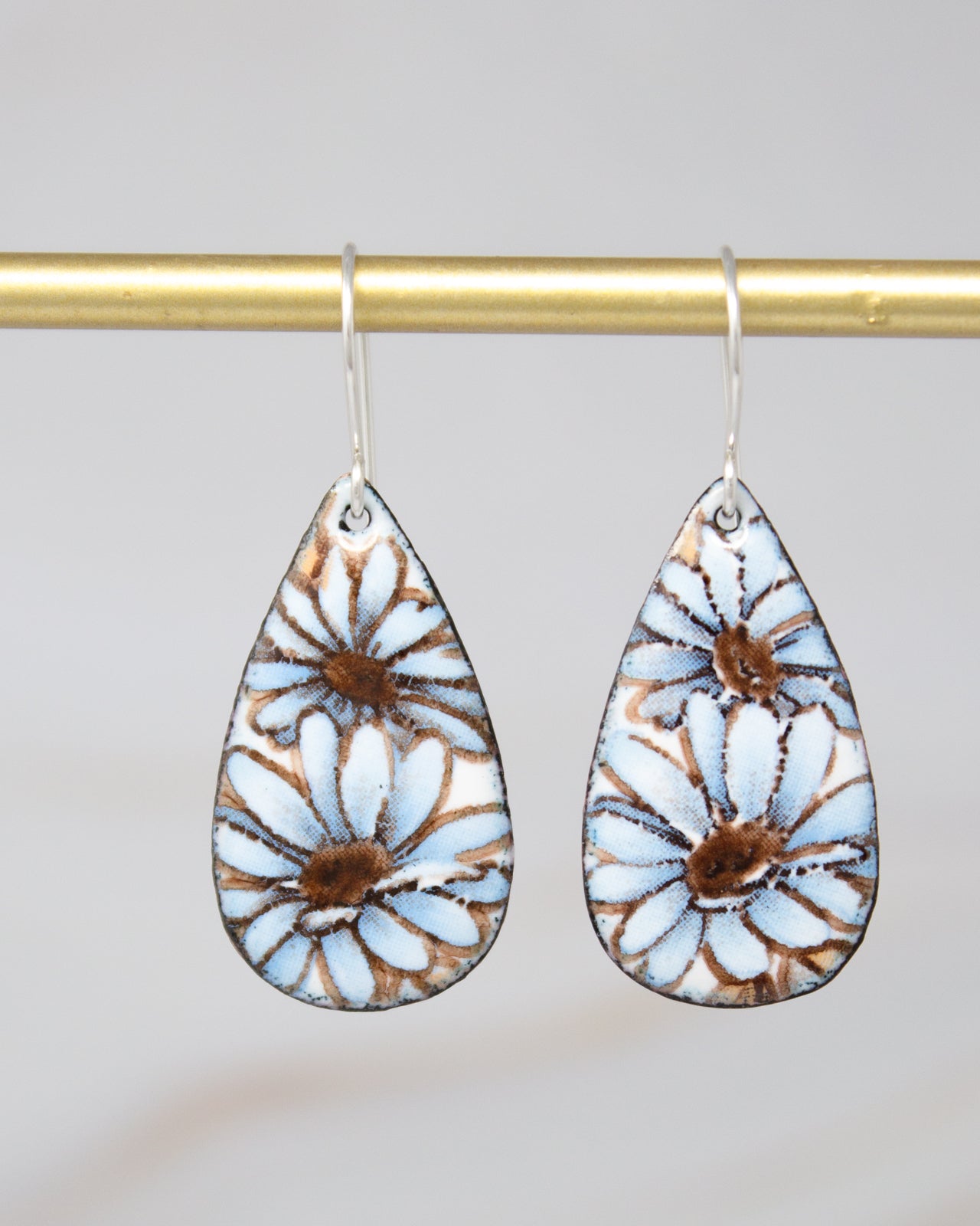A pair of earrings with blue and brown floral designs hanging from a gold bar.