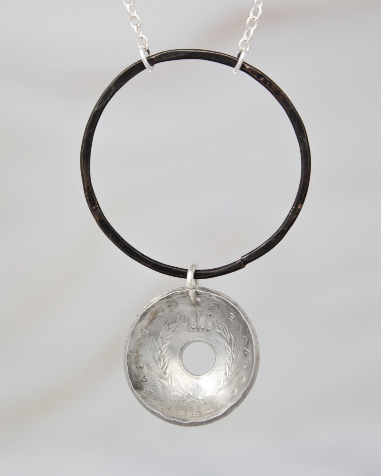 A silver pendant with a circular design hangs from a chain against a plain background.