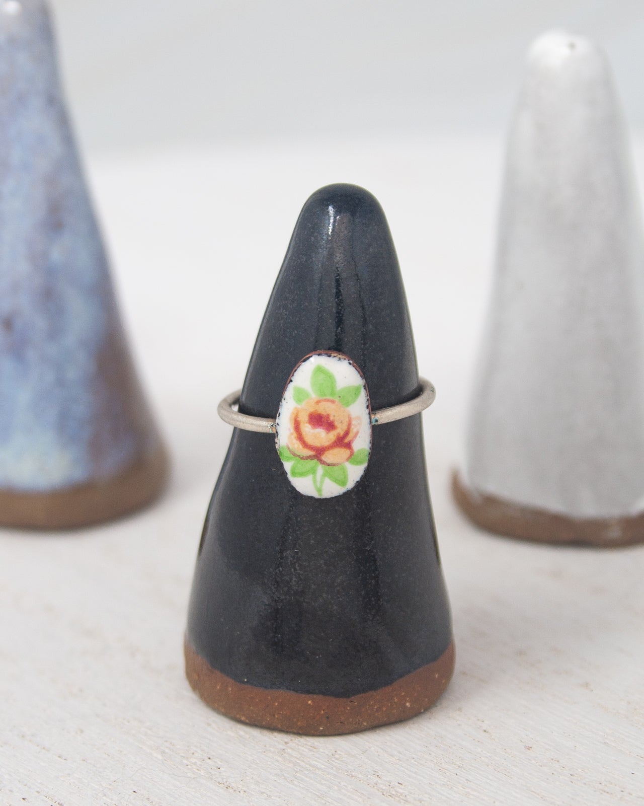 A black ceramic ring stand with a white ceramic ring on it, placed on a white surface.