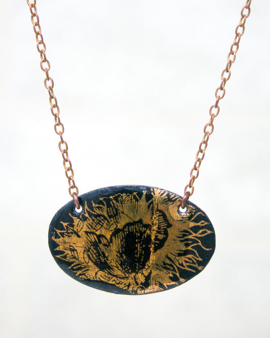 A necklace with a pendant featuring a detailed floral design in black and gold colors.