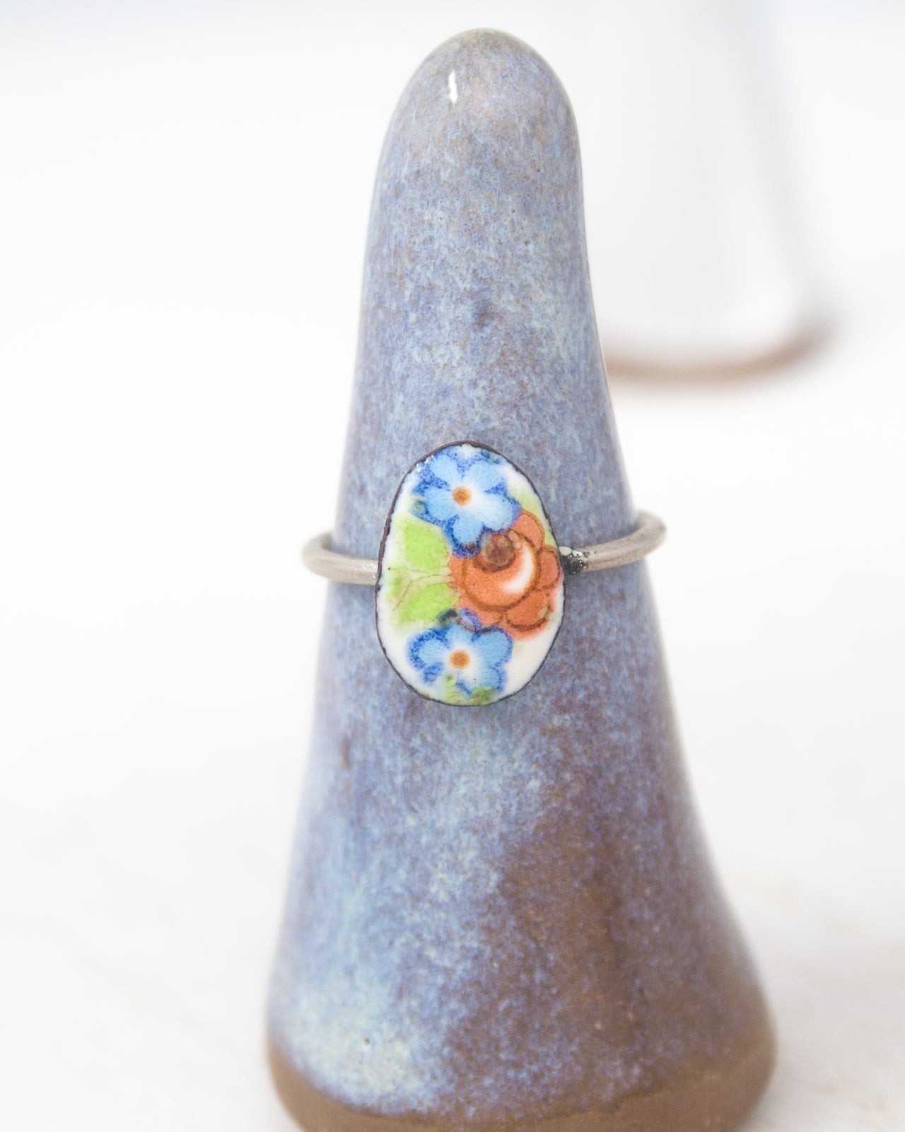 A ring with a colorful floral design on it, displayed on a ceramic stand.