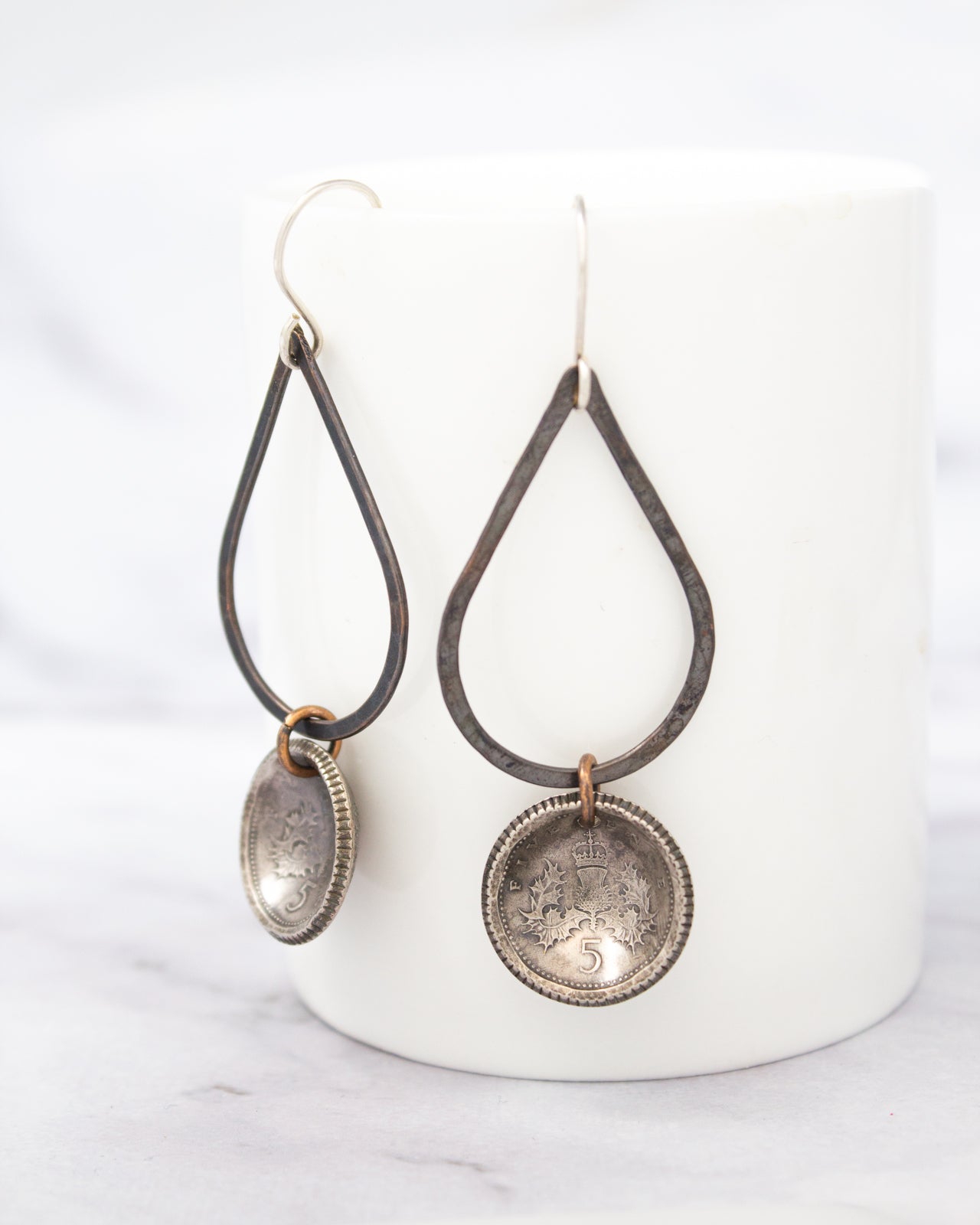 A pair of earrings with metal frames and dangling charms, one of which is a round metal coin charm.