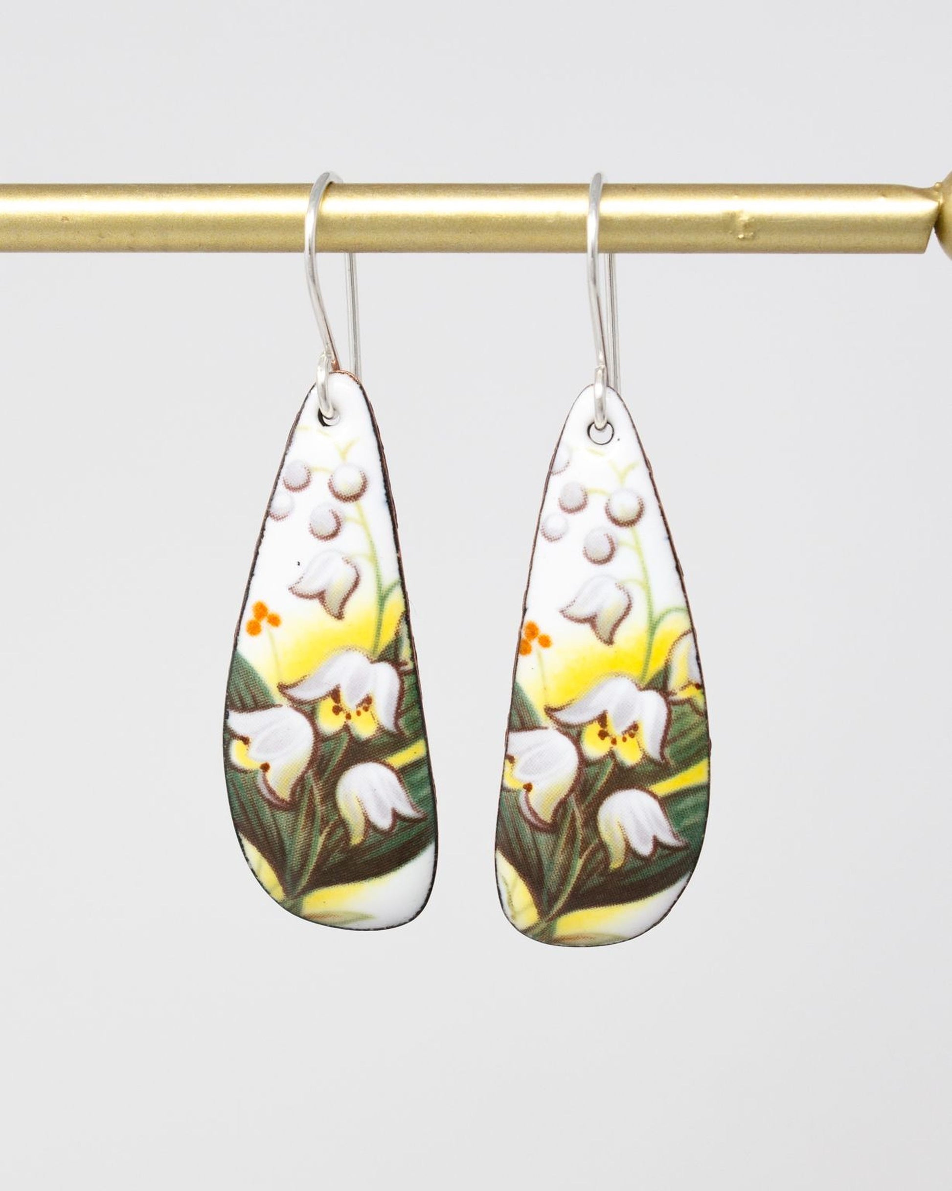 A pair of earrings with a floral design, featuring white flowers and green leaves.